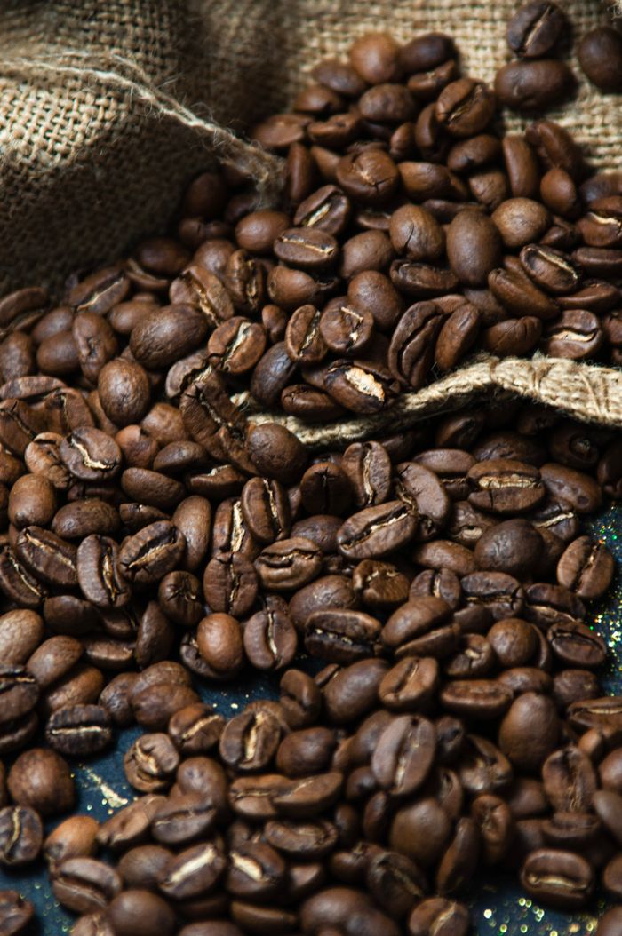 Richly roasted coffee beans spilling from burlap sack.