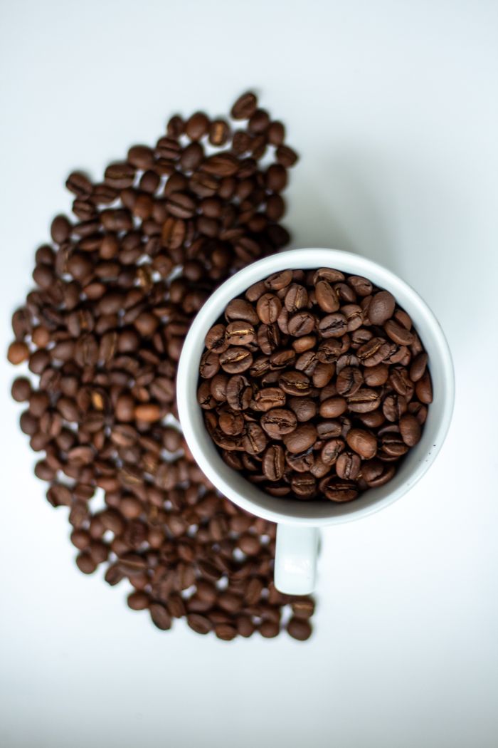 A white mug filled with coffee beans on a white surface, artistic top view.