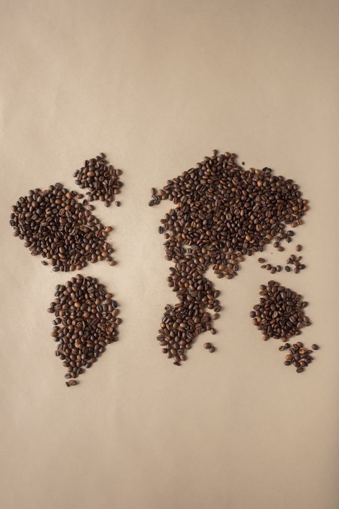 Creative flatlay of coffee beans forming a world map on beige background.